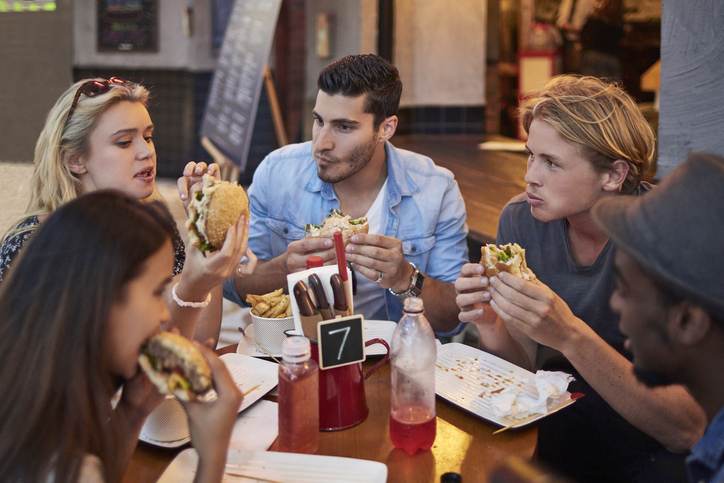 Young friends having burgers in restaurant