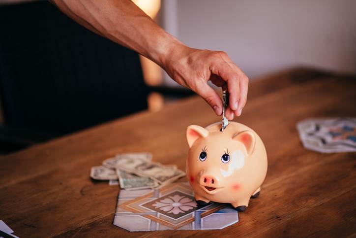 Young man saving money in a piggy bank at home